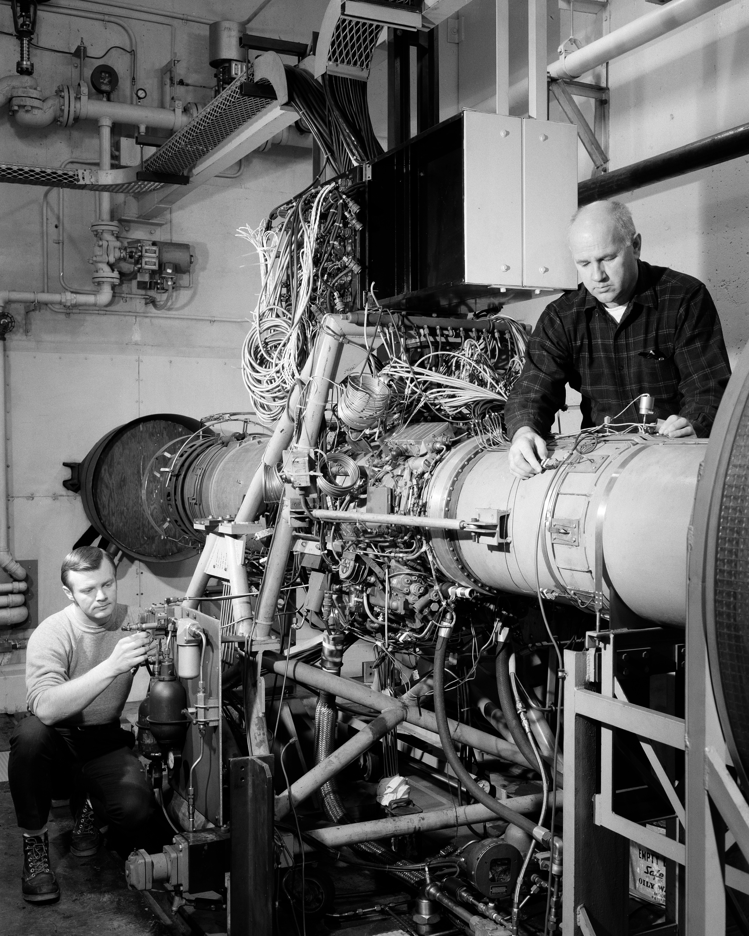 Two men instrumenting jet engine in test cell.