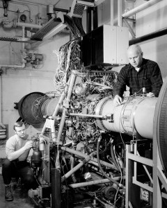 Two men instrumenting jet engine in test cell.