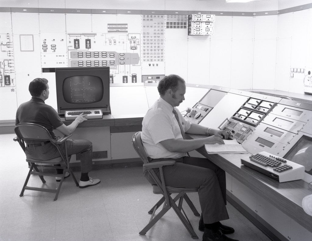Two men sitting at control panels