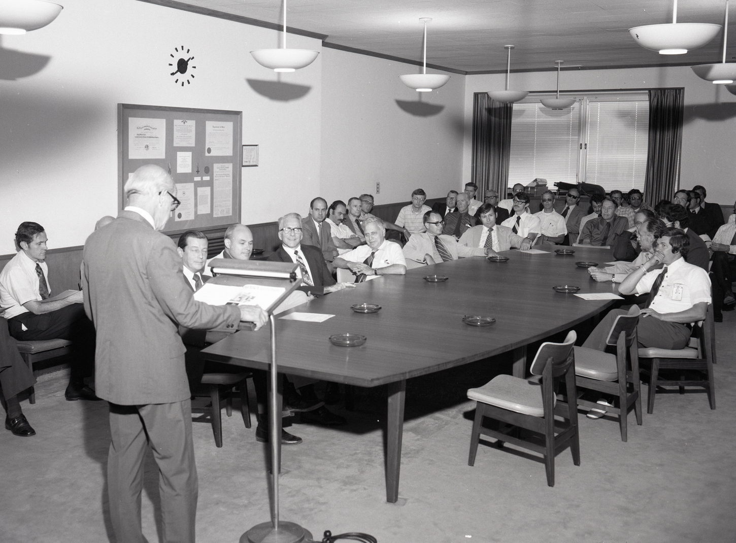 Standing man addressing people seated in conference room.
