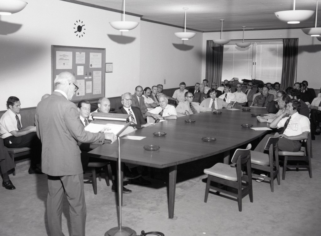 Standing man addressing people seated in conference room.