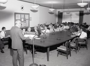 Standing man addressing people seated in conference room.