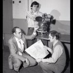 Three men looking at engine and blueprints.