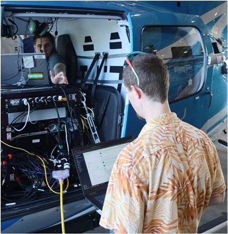 Two NASA team members prepare a computer and other hardware for a flight test aboard a helicopter.