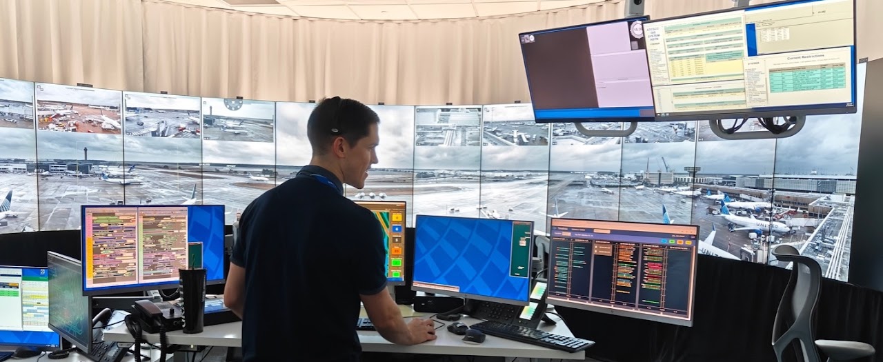 A man wearing a dark ship interacting with software while looking at multiple monitors.