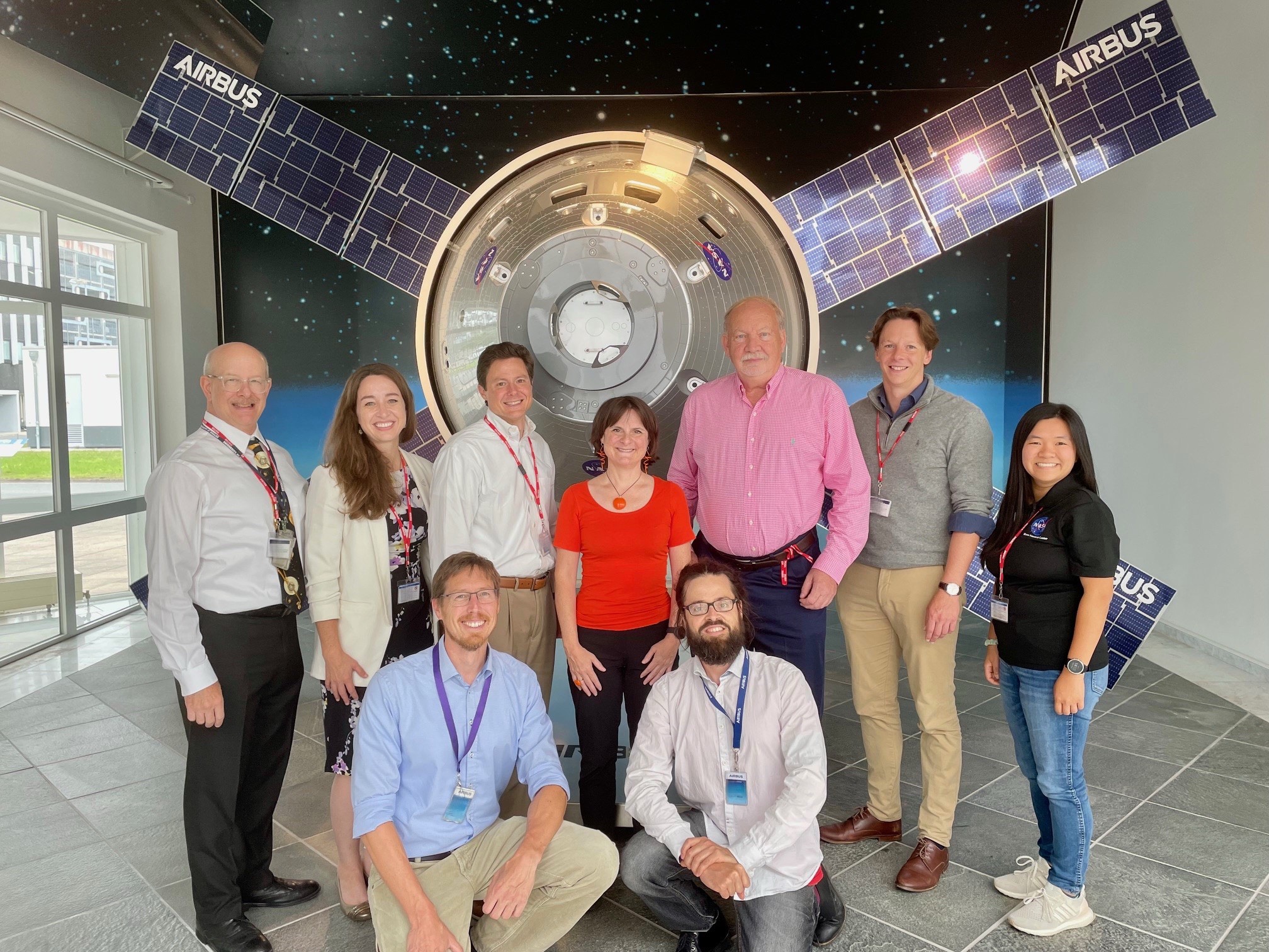 A group of nine people stand in front of a spacecraft model.
