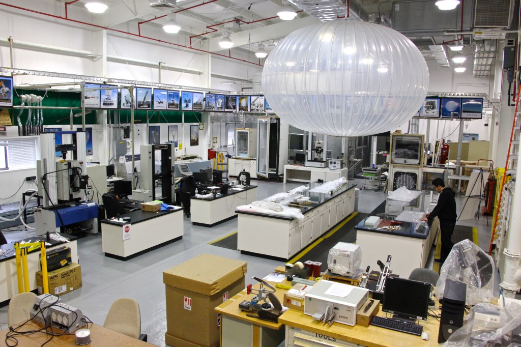 Research lab with material testing machines and tables with plastic samples. A technician prepares samples to the right of the image and centered is a display balloon.