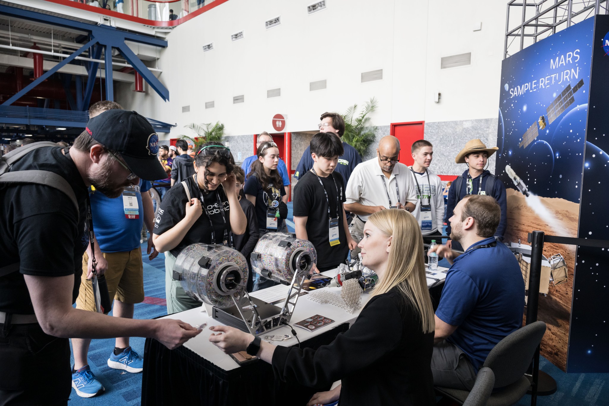Two people sit at a booth with space exploration materials. They are engaging with the public at an event.
