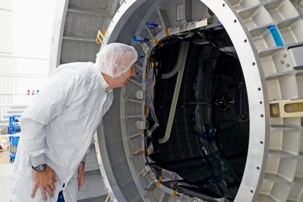 NASA astronaut Randy Bresnik, wearing a cleanroom suit and hair covering, leans forward to look into the interior of the HALO module during a facility visit at Northrop Grumman in Gilbert, Arizona. The interior and structural details of the module are partially visible.