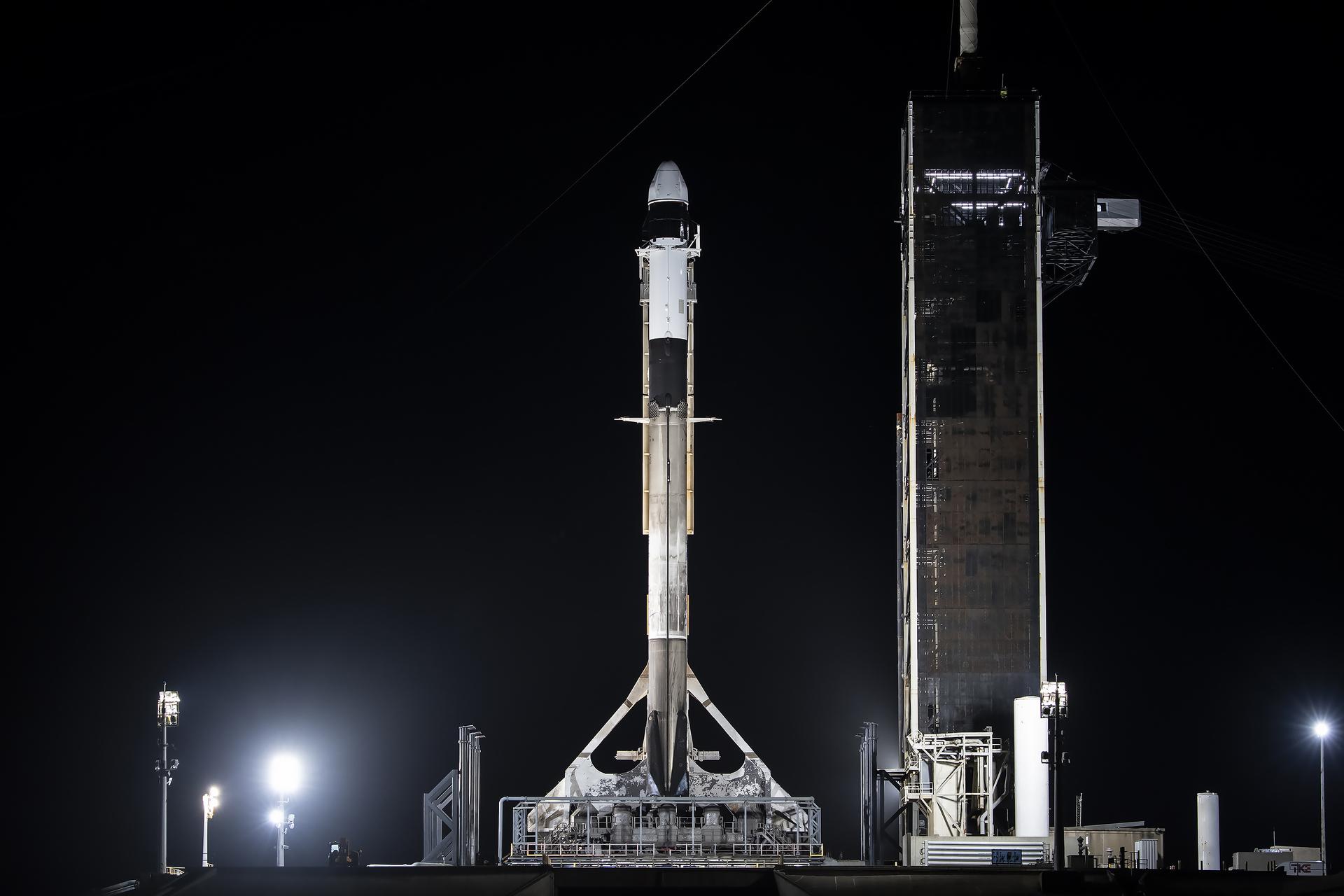 A tall black and white rocket stands ready to launch, with the night sky behind it.