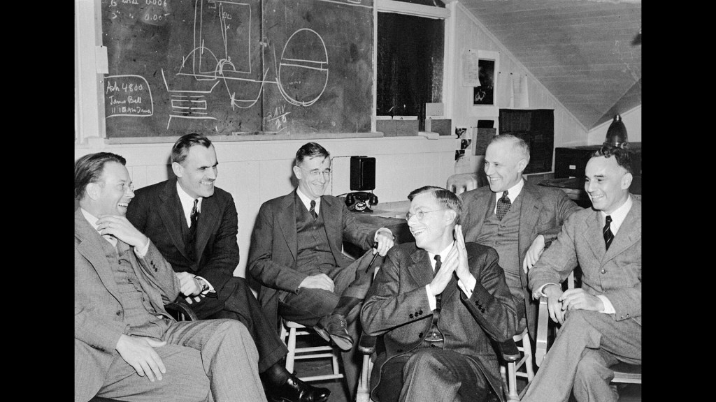Group of men sitting in front of blackboard.