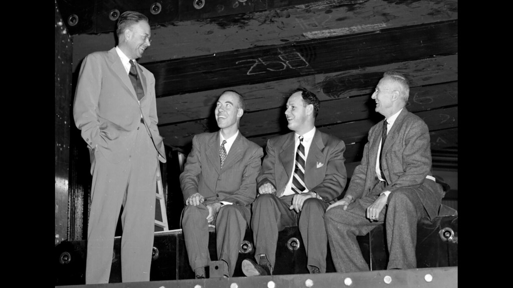 Three men seated and one standing.