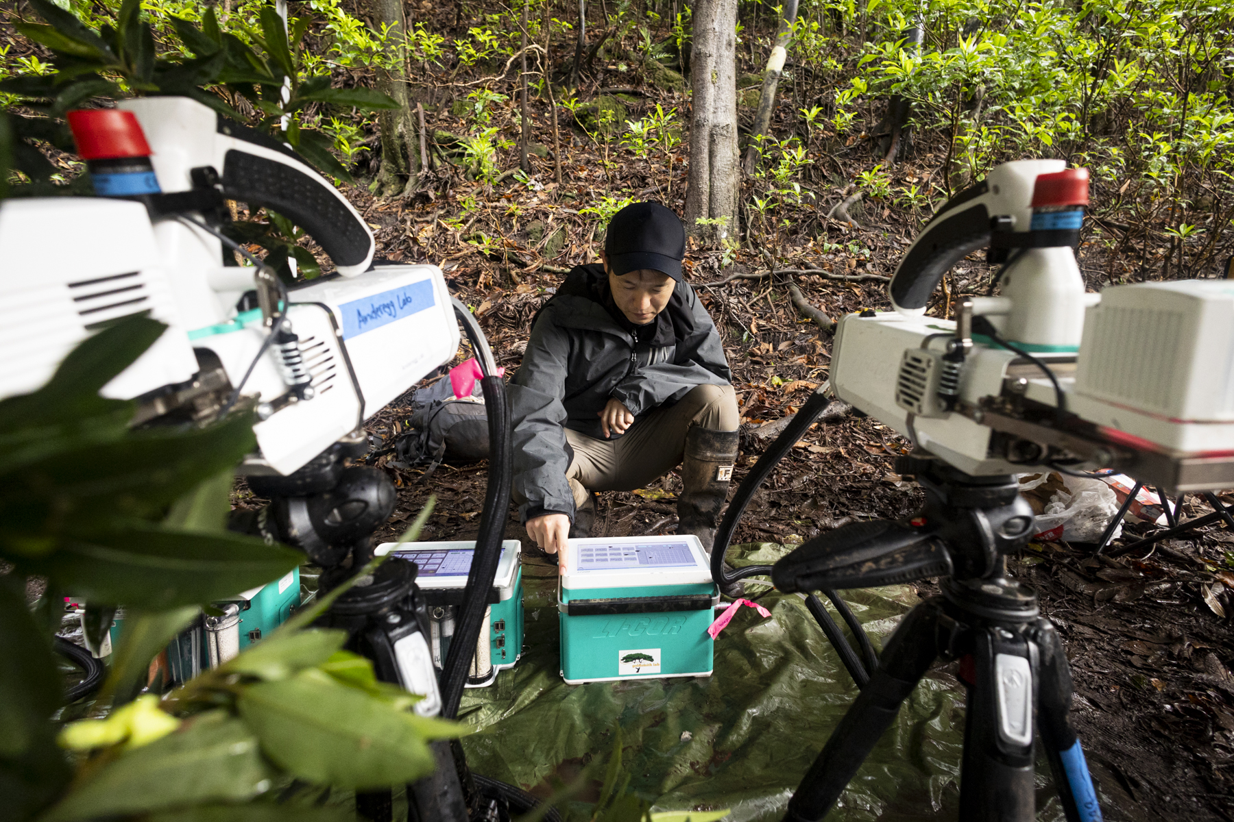 A person squats in a forest and adjusts a machine in a box while surrounded by instrumentation.