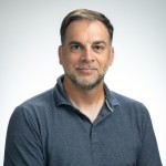Studio portrait of Michel Nuevo, a scientist at NASA Ames Research Center. He is sitting in a studio with a blue shirt.