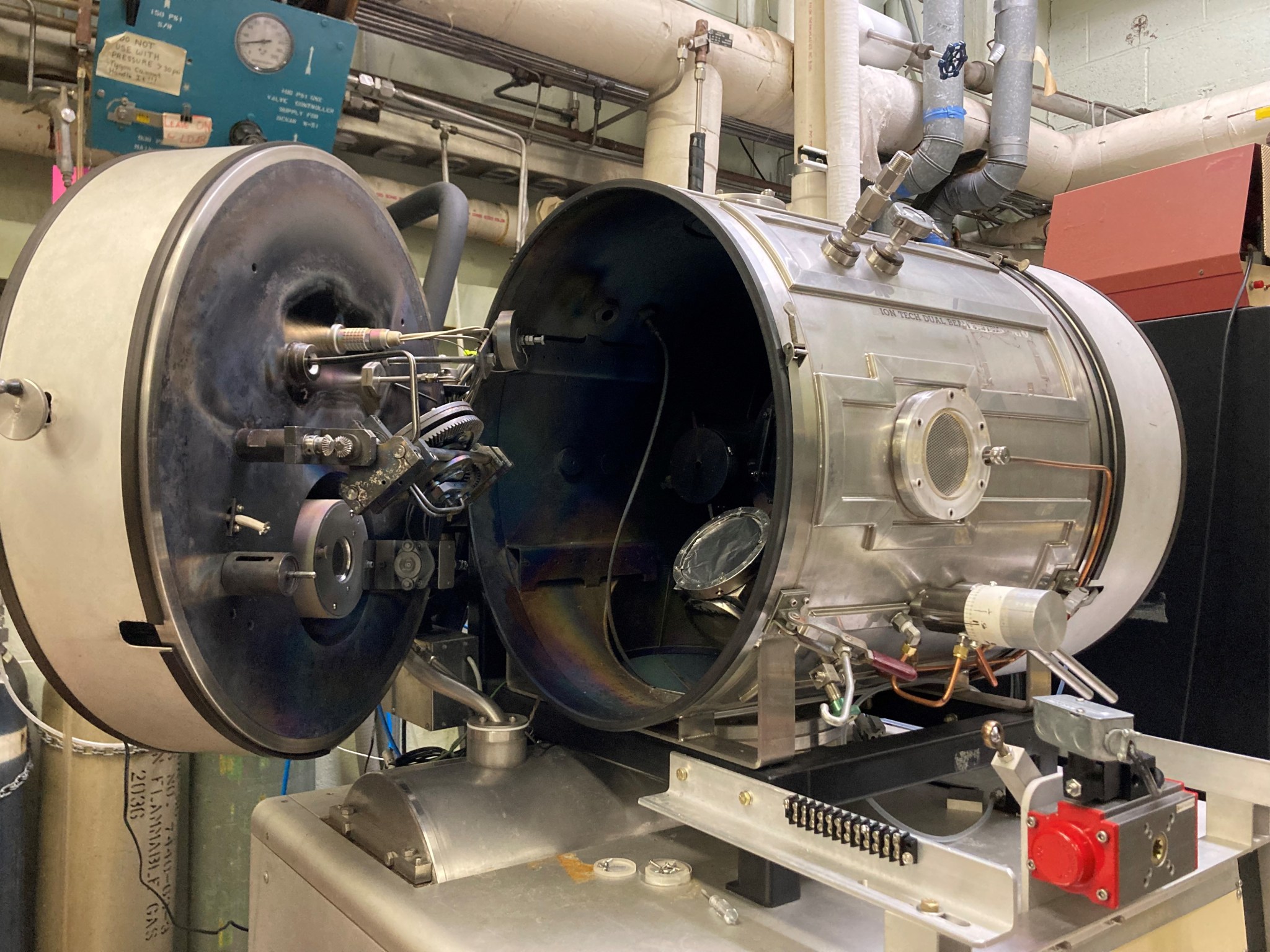 A cylindrically shaped stainless steel vacuum chamber with its door open, showing instruments and wires on the exterior and interior.