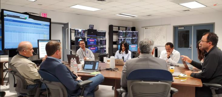 Image of 8 people sitting around a table on their laptops, with the caption "DIP Team with Wisk Aero and SkyGrid at NTX"