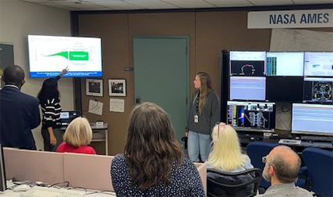 Image of a woman presenting on a tv, with 6 people watching, surrounded by computer monitors that show air traffic management software, with the caption, "Swati Saxena presenting to the ULI team"