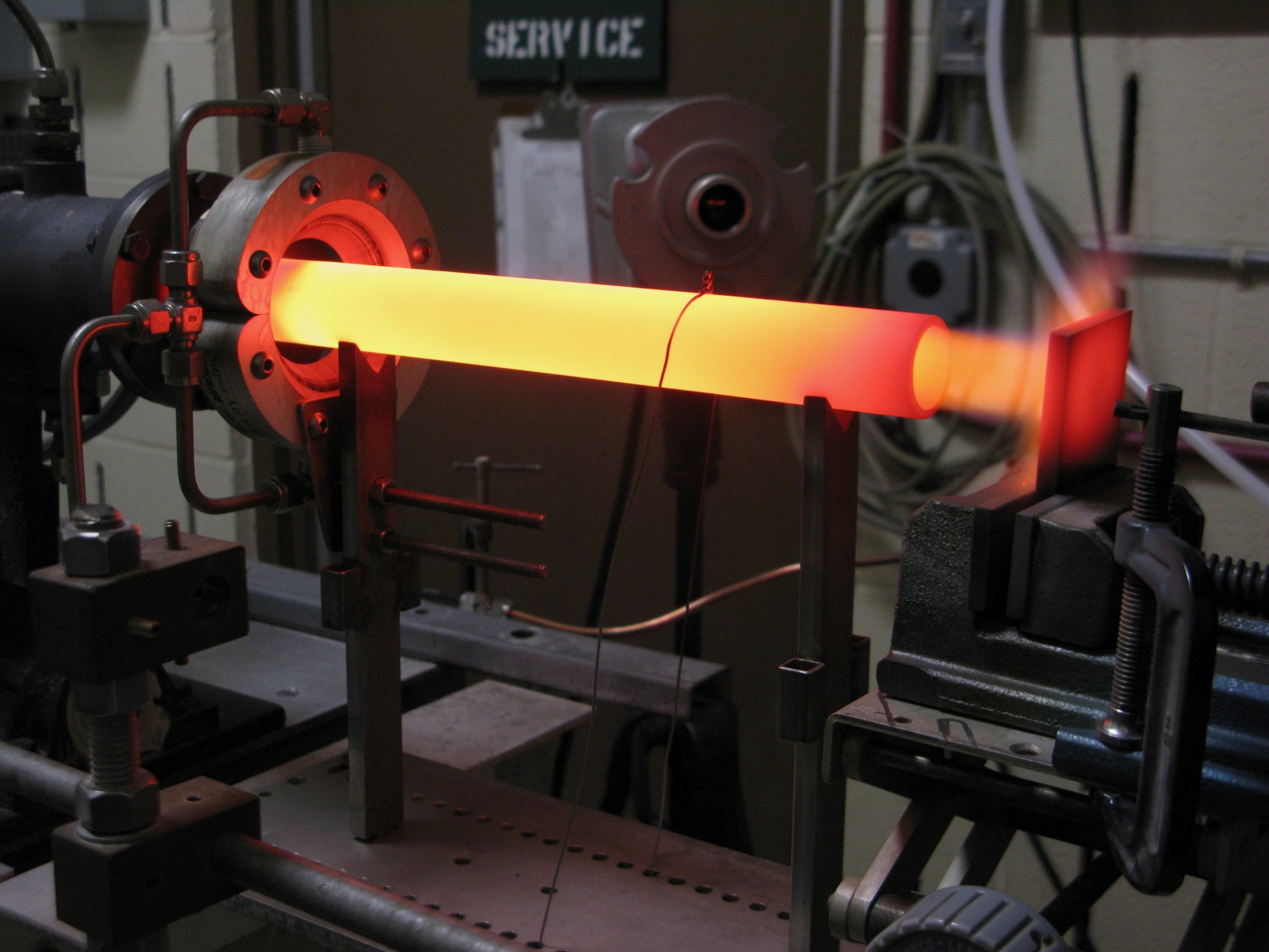 A glowing rod directs heat toward a material test coupon.