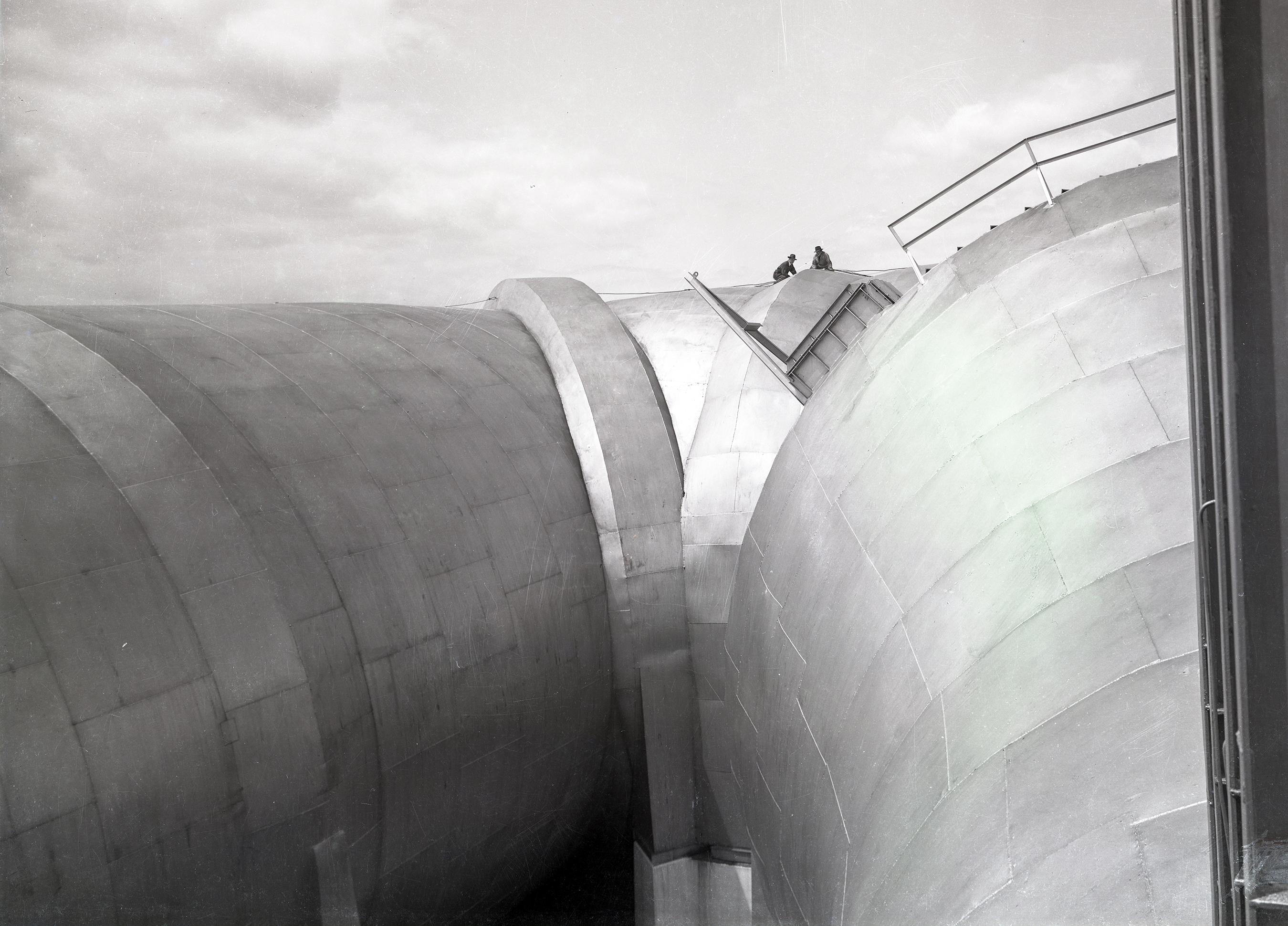 Two men atop wide end of AWT tunnel shell