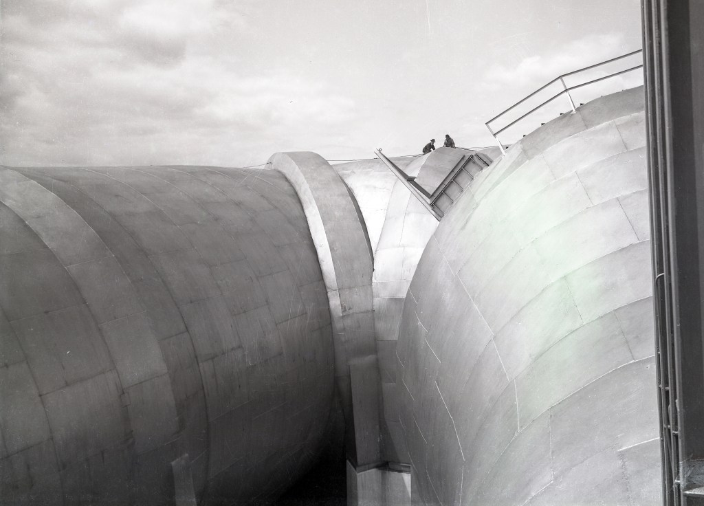 Two men atop wide end of AWT tunnel shell