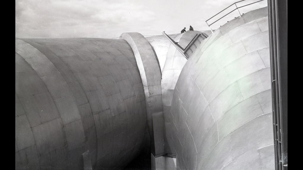 Two men atop wide end of AWT tunnel shell