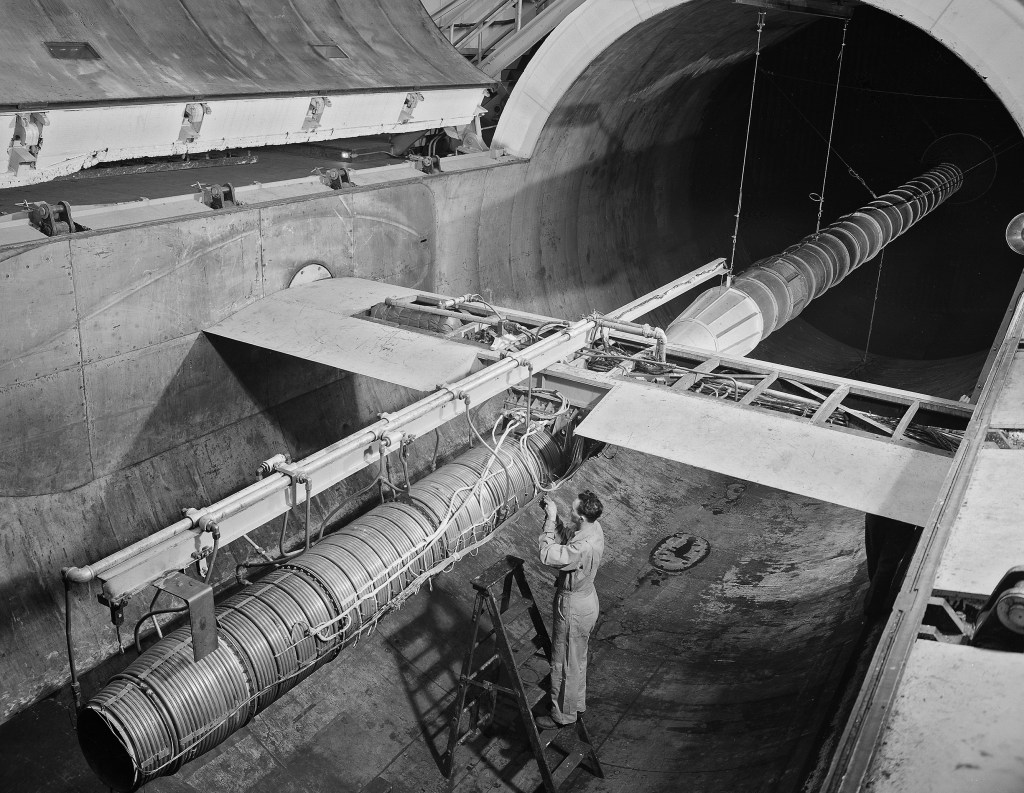 A mechanic stands beside ramjet engine in AWT test section