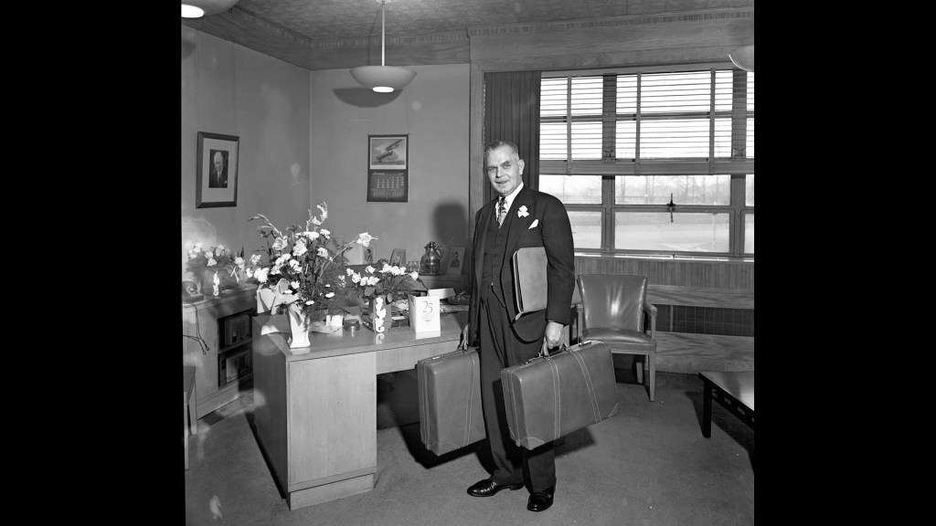 Man standing with suitcase in office.