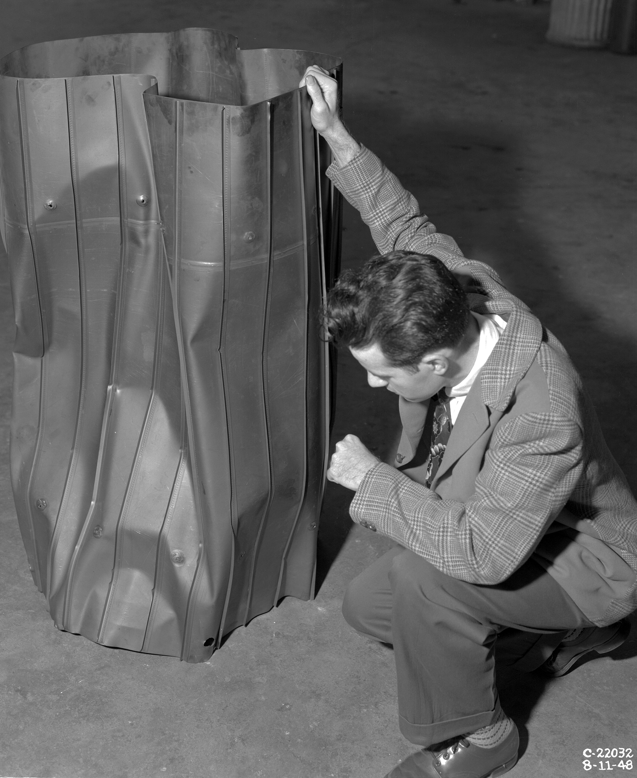 Kneeling researcher examines steel liner in shop area.