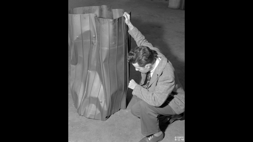 Kneeling researcher examines steel liner in shop area.