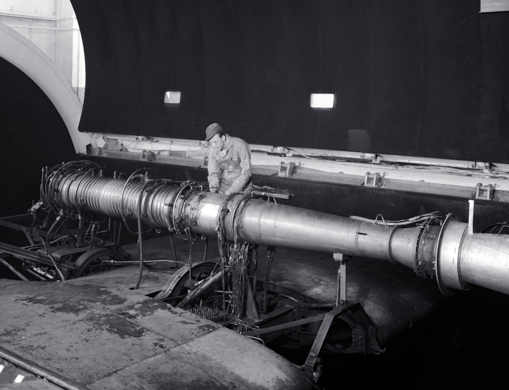 A mechanic stands beside ramjet engine in AWT test section