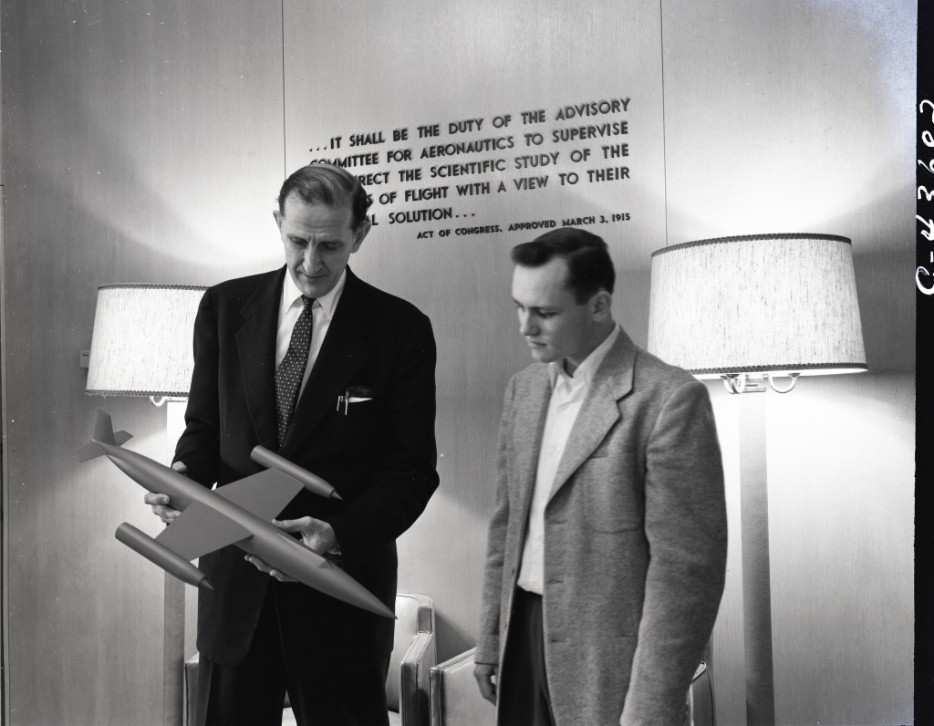 Two men looking at aircraft model with lamps in background.