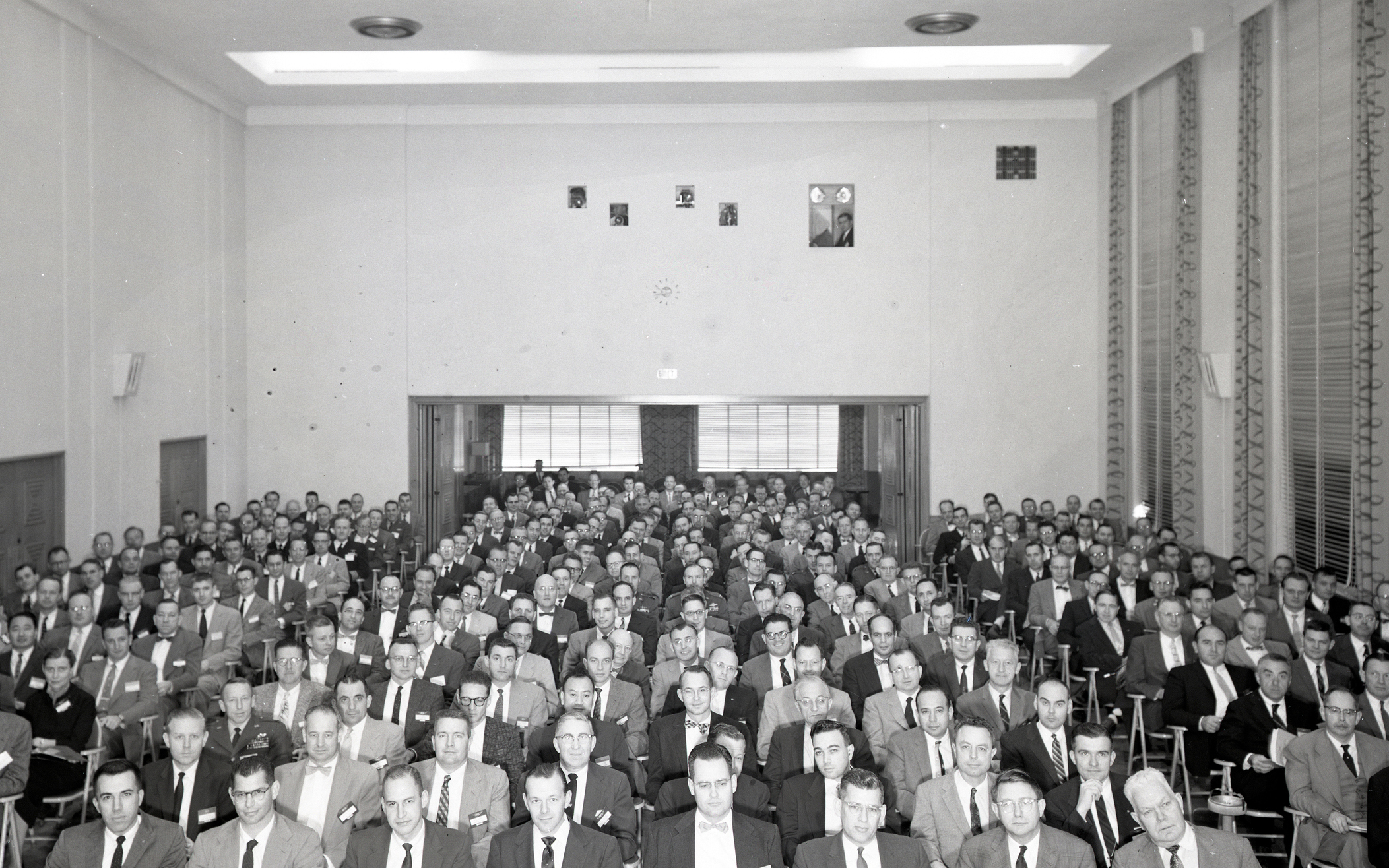 People seated in auditorium and foyer in background.