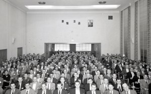People seated in auditorium and foyer in background.