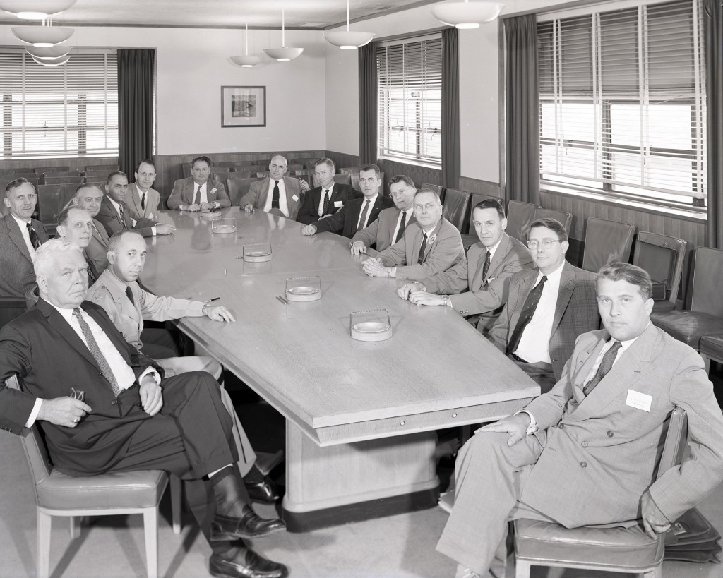Group of men seated at conference table.