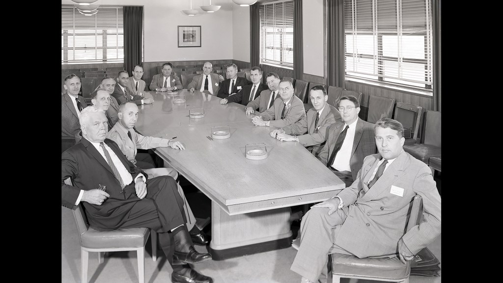 Group of men seated at conference table.