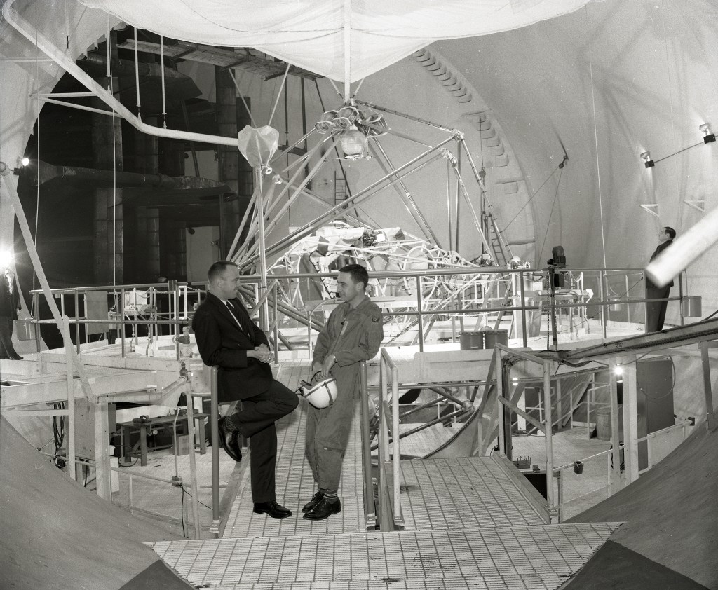 Two men talking with test rig in background.
