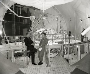 Two men talking with test rig in background.