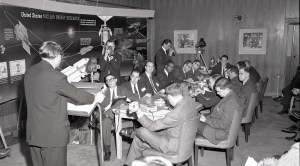 Man addressing people seated at table.