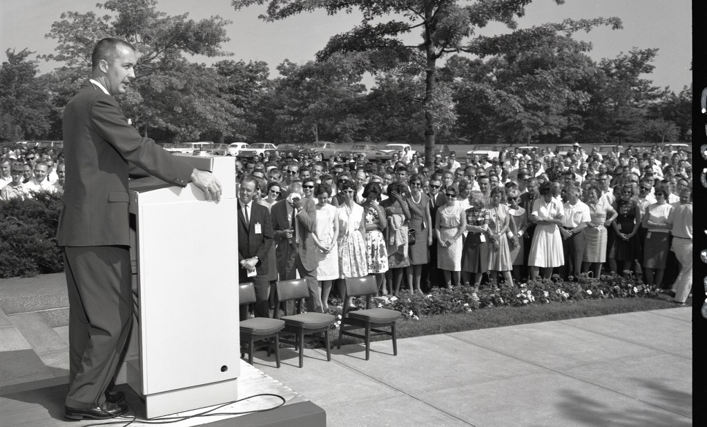 Man speaking to crowd outside building.