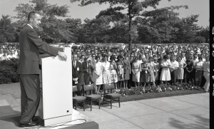 Man speaking to crowd outside building.