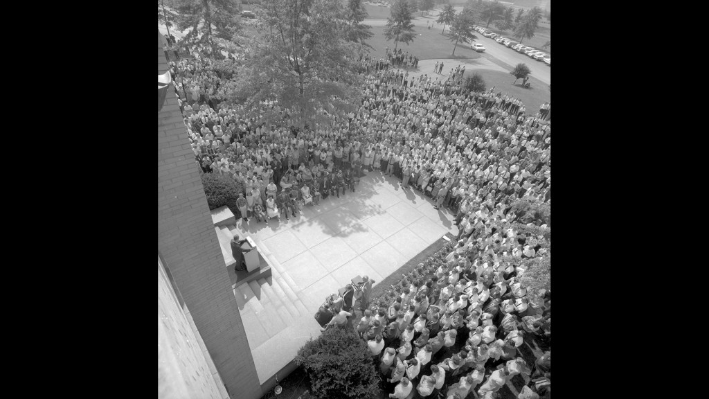View down onto crowd outside building listening to speaker.