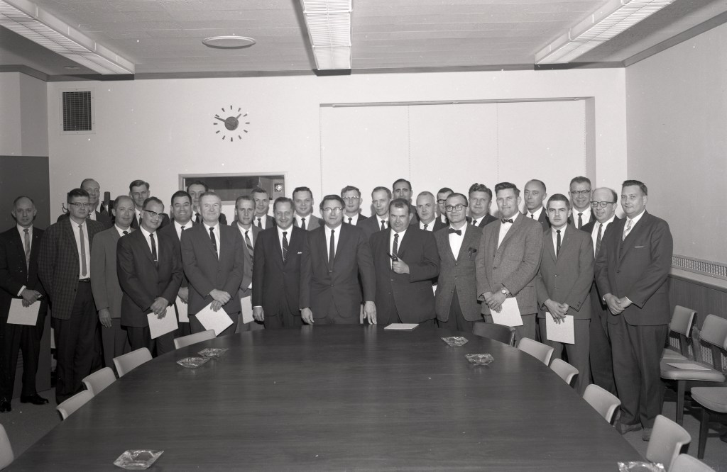 Group of men standing at end of table.