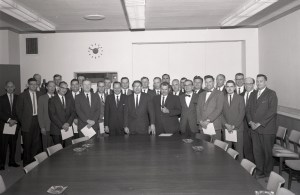 Group of men standing at end of table.
