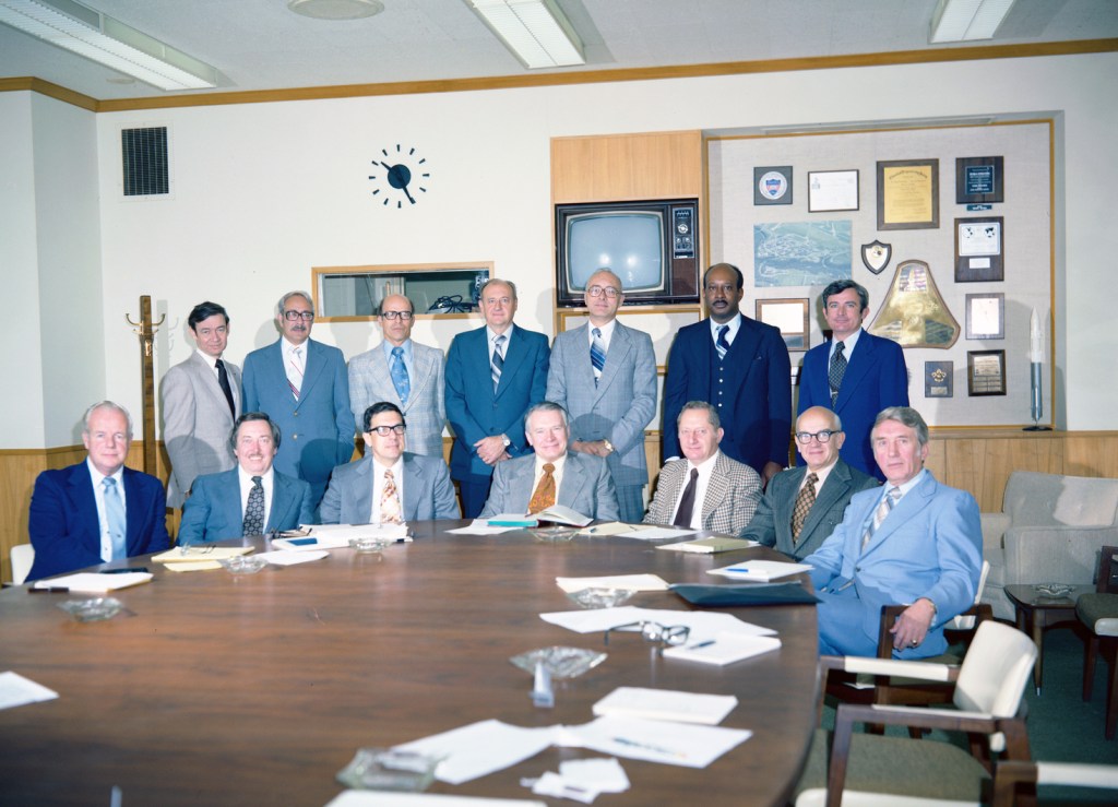 Group of men standing at end of table.
