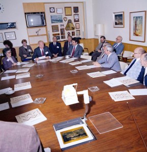 People sitting around oval conference table.