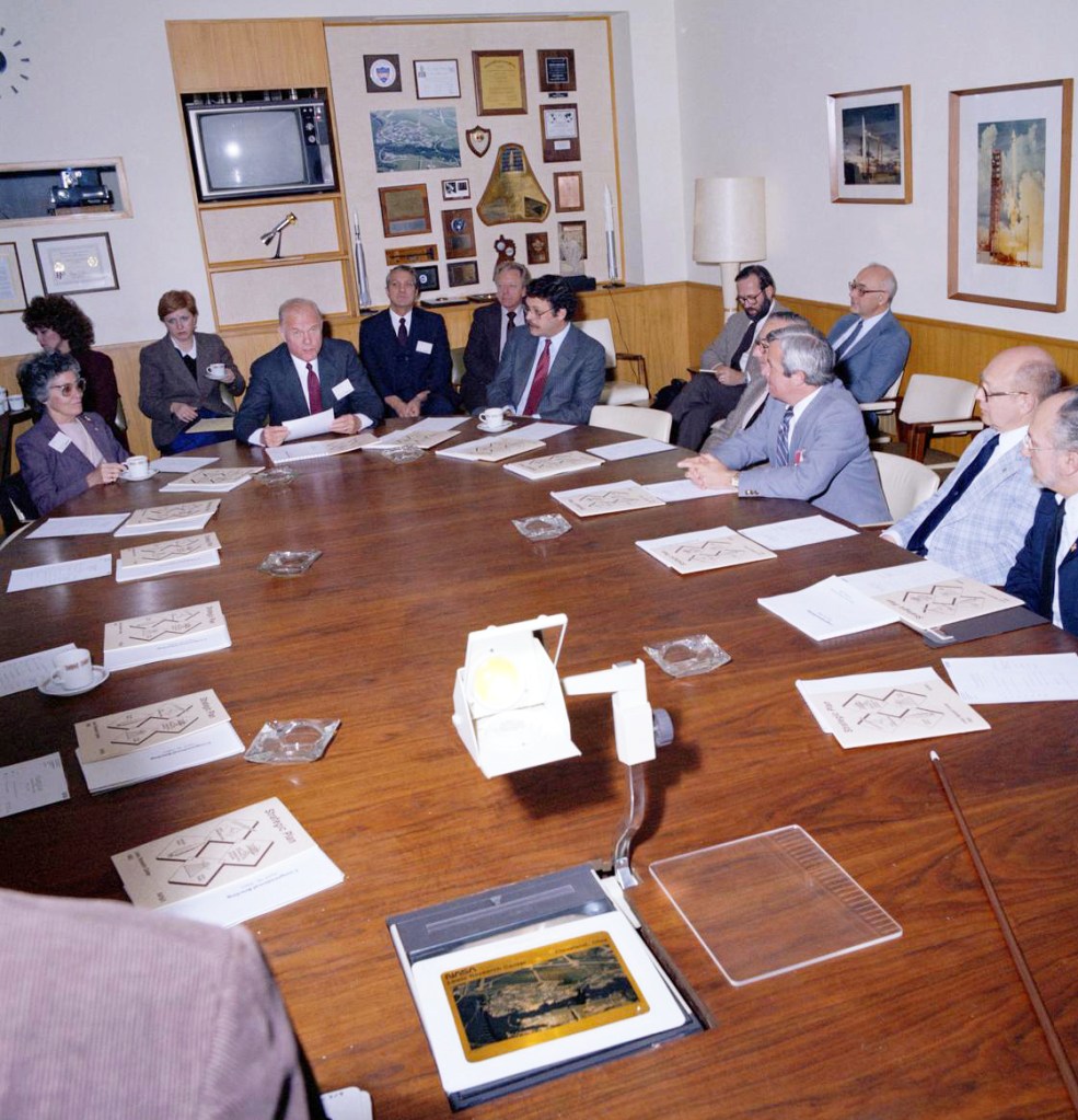 People sitting around oval conference table.
