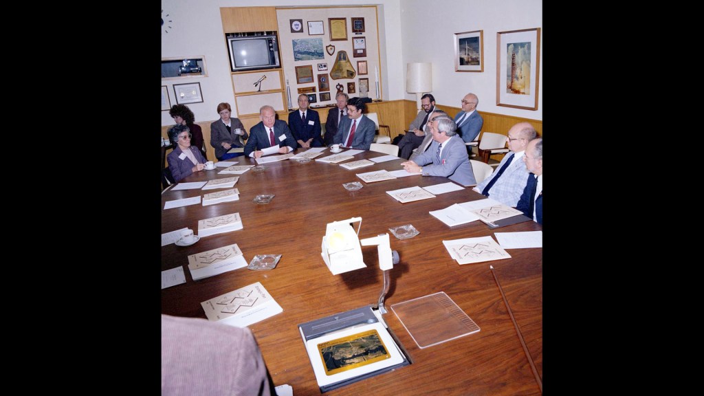 People sitting around oval conference table.