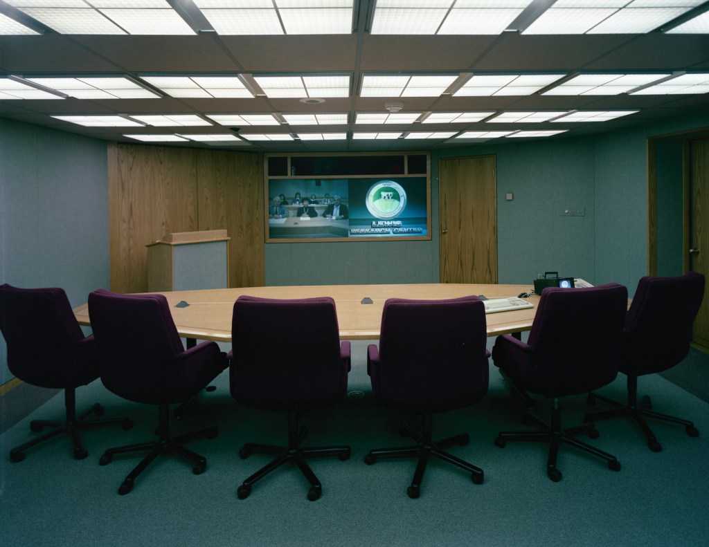 Table with chairs in front of wall-mounted screens.