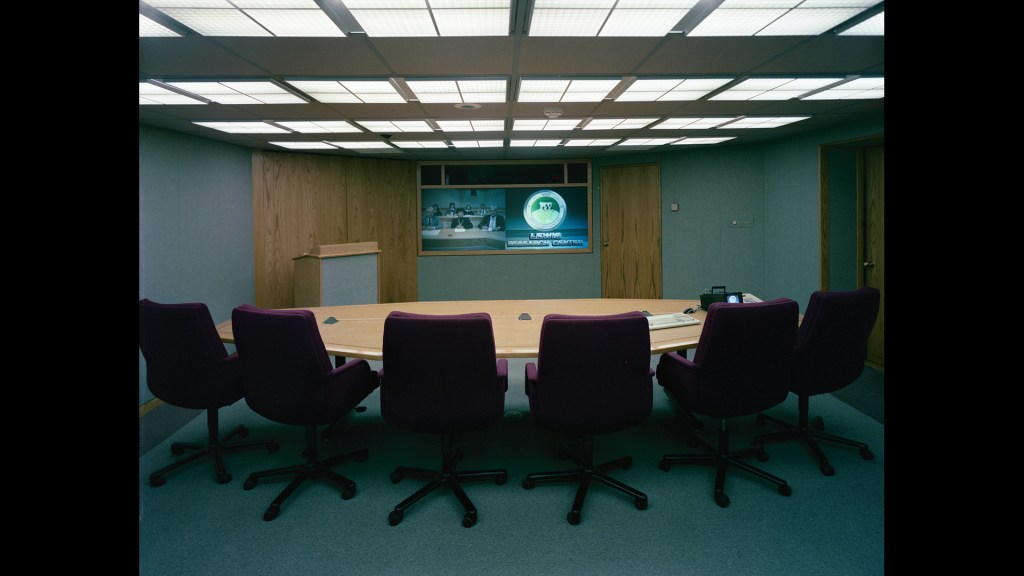 Table with chairs in front of wall-mounted screens.