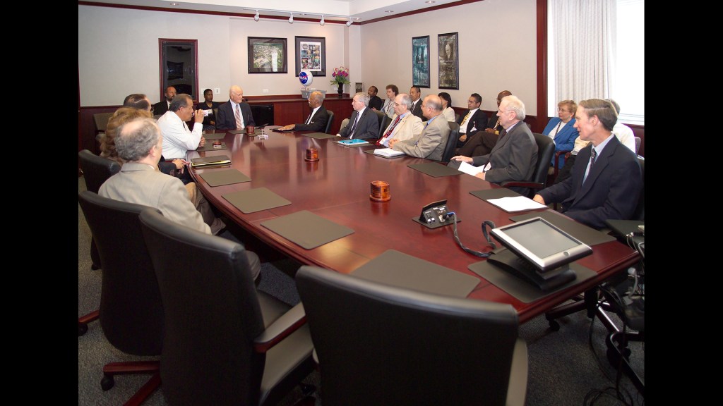 People sitting around oval conference table.